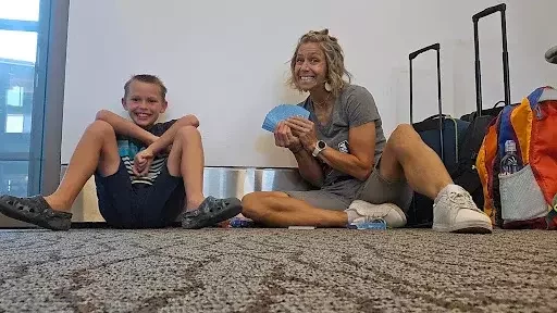 Noelle and her son Makai sitting on an airport floor holding some "go fish" cards.